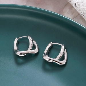 Boucles d'oreilles créoles argentées irrégulières sur une assiette en porcelaine
