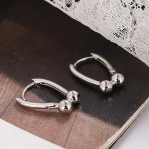Minimalist silver U-shaped hoop earrings with metal beads on a lace and magazine background