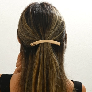 Detail of a matte gold punk metal ponytail clip worn on dark hair with a minimalist style