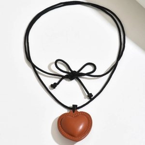 Dettaglio macro del ciondolo a cuore in pelle con cuciture e collana con fiocco