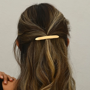 Minimalist gold bar spring hair clip shown on wavy brown hair in a half-up hairstyle