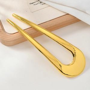 Close-up of a minimalist U-shaped gold metal hair pin on a light wooden tray