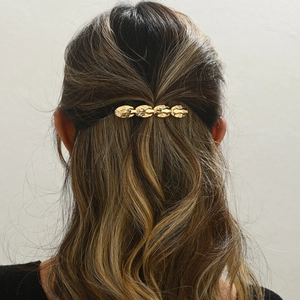 Détail d'une pince à cheveux dorée en métal texturé sur la coiffure d'un mannequin