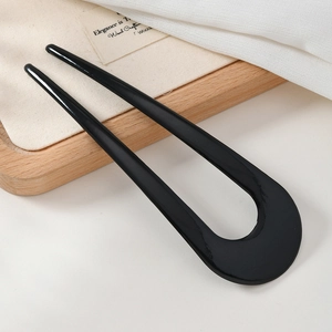 Close-up of gloss black U-shaped hair pin on rustic wooden tray and linen cloth