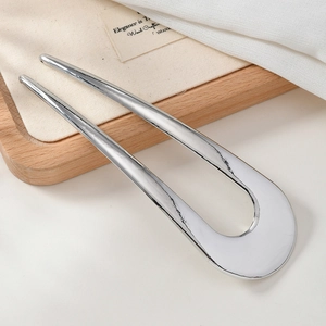 Close-up of polished silver U-shaped hair fork on a wooden tray with linen background