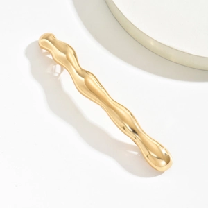 Détail macro de la barrette dorée ondulée avec une finition métallique polie et brillante