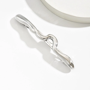 Détail d'une barrette argentée ondulée avec finition en métal liquide poli sur fond blanc