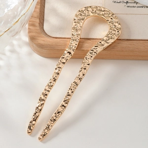 Close-up of golden U-shaped hair pin with hammered texture on white velvet pouch