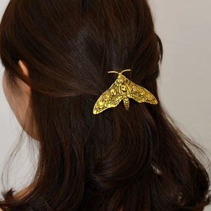 Detailed view of a vintage gold moth hair clip styled on dark brown hair in a natural setting