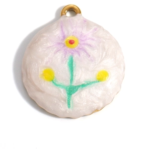 Macro detail of a round 18K gold-plated flower pendant with purple petals and green leaves