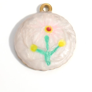 Detail of flower enamel charm in 18K gold plated finish with creamy white background