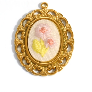 Macro shot of oval gold-plated pendant featuring delicate floral hand embroidery detail