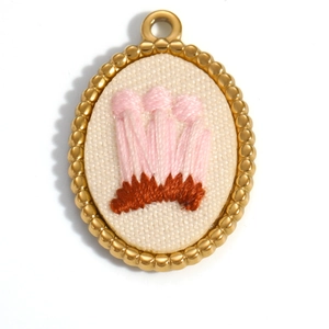 Macro detail of oval gold pendant with handmade mushroom embroidery on white fabric
