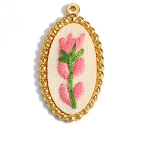 Detailed macro view of an oval 18K gold pendant with pink floral embroidery and white fabric