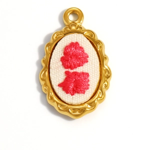 Detailed close-up of 18K gold plated oval pendant with hand-stitched red flowers