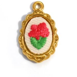 Macro view of floral embroidery on 18K gold plated oval pendant with wave border