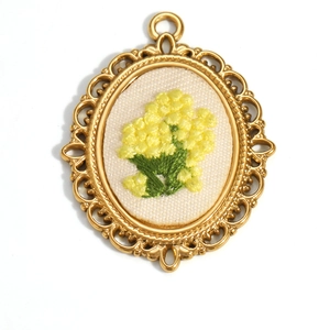 Detailed macro view of an oval 18K gold plated flower embroidery pendant on white background
