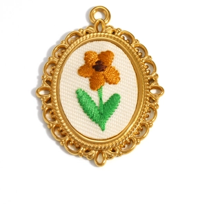 Macro detail of oval floral embroidery pendant with gold plated stainless steel frame