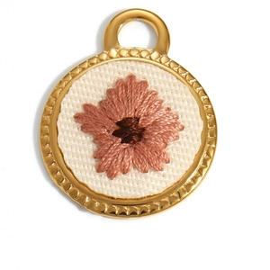 Macro shot of 18K gold plated oval flower charm with detailed embroidery on linen fabric