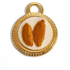 Macro detail of 18K gold-plated oval pendant featuring intricate yellow floral embroidery