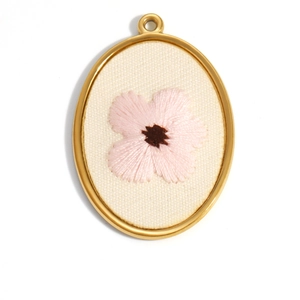 Macro view of 18K gold-plated oval pendant with floral embroidery and white fabric