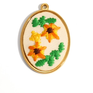 Detailed embroidery of orange sunflowers on an oval 18K gold plated jewelry pendant