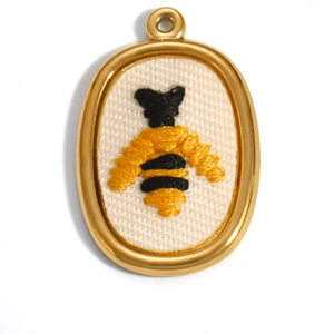Macro shot of 18K gold-plated oval pendant featuring detailed bee embroidery on canvas
