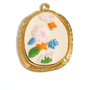 Detailed macro view of 18K gold plated oval pendant with colorful floral embroidery