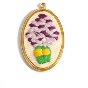 Detail of oval 18K gold plated stainless steel floral embroidery pendant with purple flowers