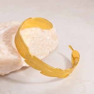 Detailed close-up of golden feather-shaped open bangle on white crystal base