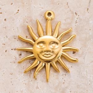 Macro d'un pendentif soleil doré avec rayons sur un fond beige à texture rugueuse