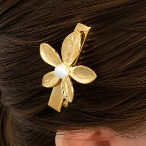 Detail einer goldenen Blumen-Haarklammer mit Perle auf dunklem Haar mit Textur