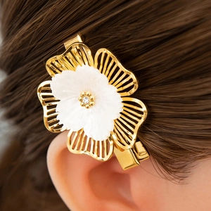 Detailed close-up of a golden flower hair clip with shell-like petals and crystal core