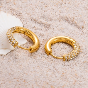 Boucles d'oreilles créoles dorées 18k avec strass brillants sur un fond de sable blanc