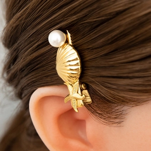 Detail of a golden seashell and pearl hair clip worn on wavy brown hair