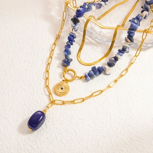 Detail of layered 18k gold plated necklaces with blue stones and sun pendant charms