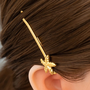 Detailansicht einer goldenen Seestern-Haarklammer mit Textur auf braunem Haar