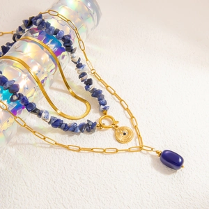 Macro detail of 18k gold-plated layered necklaces with navy blue stones on a crystal stand