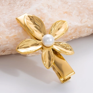 Nahaufnahme der goldenen Edelstahl-Blumenhaarklammer mit weißem Perlendetail auf Stein