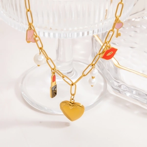 Détail du collier doré avec charms cœur, rouge à lèvres et bottines sur verre