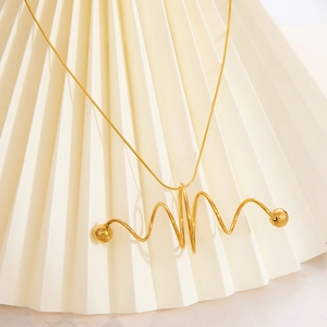 Detail of 18K gold wave spiral pendant necklace on a minimalist cream paper fan background