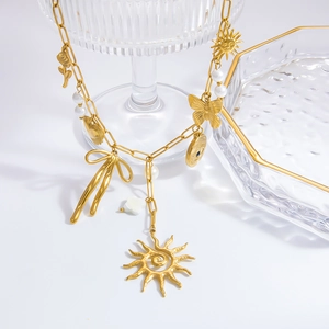 Detail of 18k gold necklace featuring sun, butterfly, and pearl charms on glass
