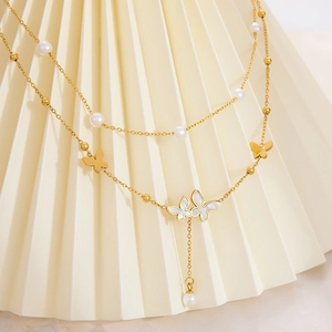 Detail of layered gold necklace featuring pearl beads and double butterfly pendants