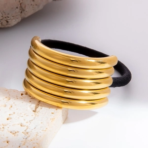 Makrodetail eines goldenen Metallrings auf schwarzem Haargummi vor schlichtem Steinhintergrund