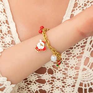 Detalle de pulsera navideña dorada con colgante de Papá Noel esmaltado y perla blanca