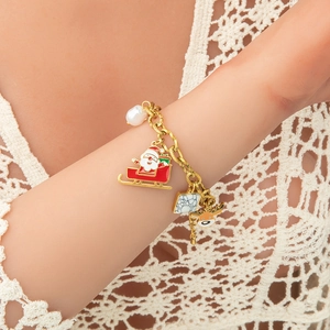 Detalle de pulsera navideña con trineo de Santa, renos y perla en cadena de metal dorado