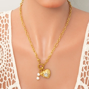 Dettaglio della collana dorata con ciondolo a cuore, lettera K e perle su pizzo bianco