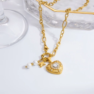 Dettaglio ciondolo a cuore dorato con zircone, lettera K e perle su catena a maglie