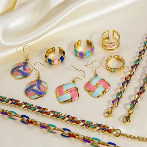 Close-up of colorful enamel jewelry set on beige satin with 18k gold rings and earrings