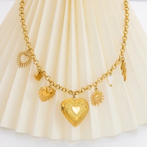 Detail einer goldenen Charm-Halskette mit Herz-Medaillon auf weißem gefaltetem Fächer